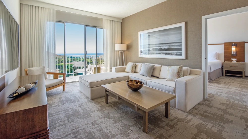 Helles Wohnzimmer mit weißem Sofa, Holztisch, großem Fenster mit Meerblick und angrenzendem Schlafzimmer.