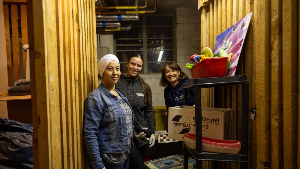 Three women standing in a storage room, surrounded by boxes and shelves of toys.