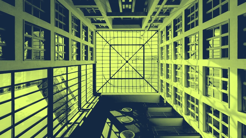 Blick nach oben in einen modernen Innenhof mit Glasdach und symmetrischen Fenstern, in Grün- und Gelbtönen gefärbt.