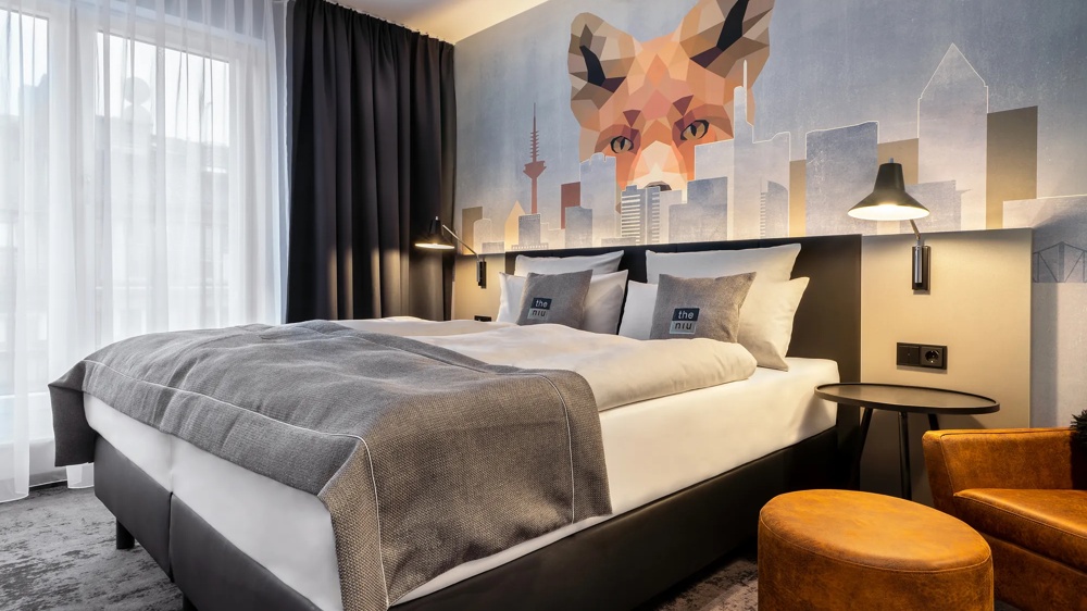 Modernes Hotelzimmer mit großem Bett, Fuchs-Wandbild, grauen Vorhängen und stilvollen Lampen.