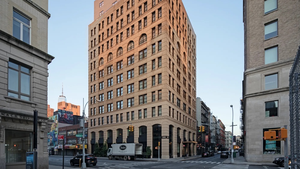 Ein großes, rotes Backsteingebäude an einer Straßenecke, umgeben von weiteren Gebäuden bei klarem Himmel.