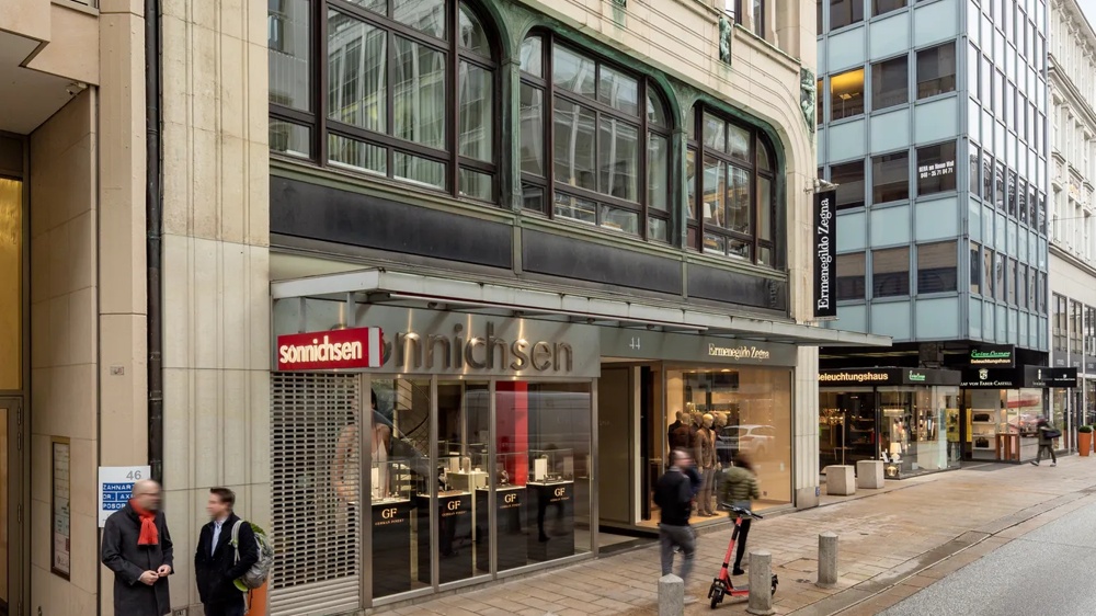 Mehrstöckiges Gebäude mit historischer Fassade, großen Fenstern und Geschäften im Erdgeschoss in einer belebten Straße.