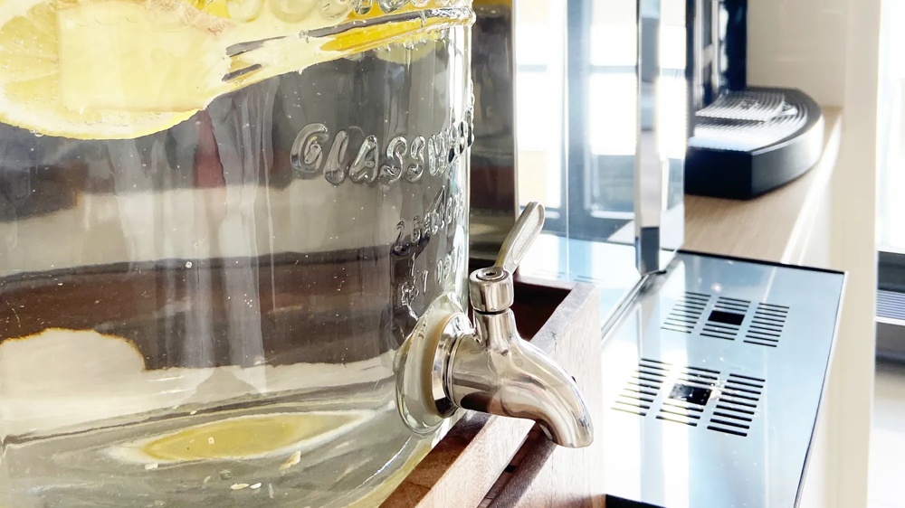 A glass container with water and lemon slices, equipped with a metal tap.