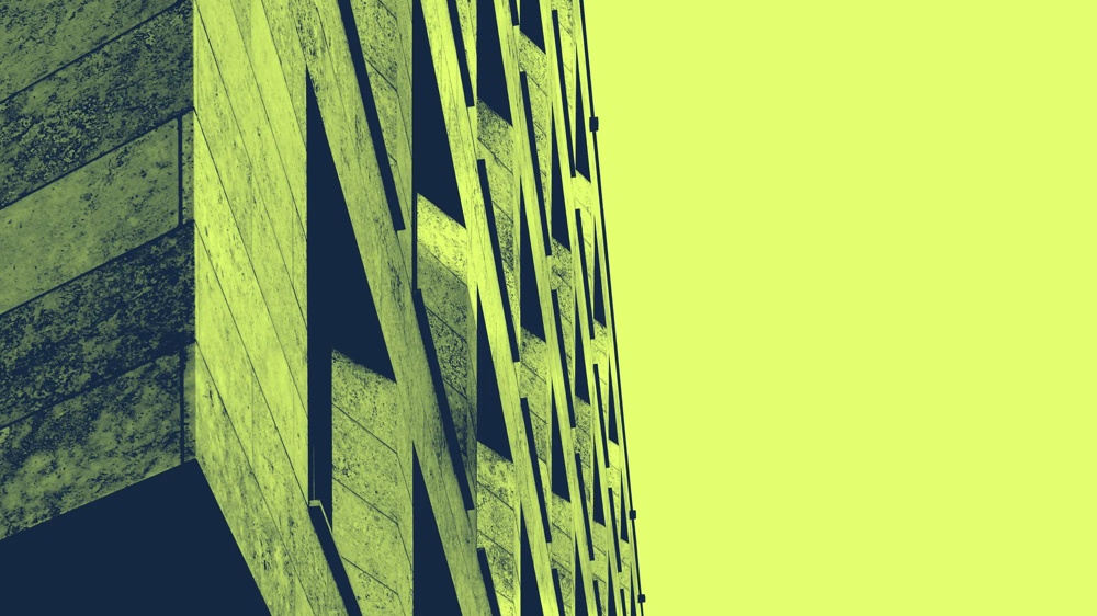 Fassadenansicht eines Gebäudes mit geometrischen Mustern vor einem hellgelben Himmel.