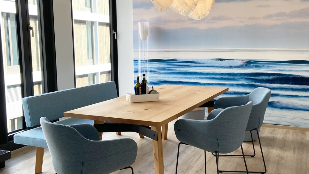 A wooden table with blue chairs in front of a wall with a sea scene and hanging lamps.
