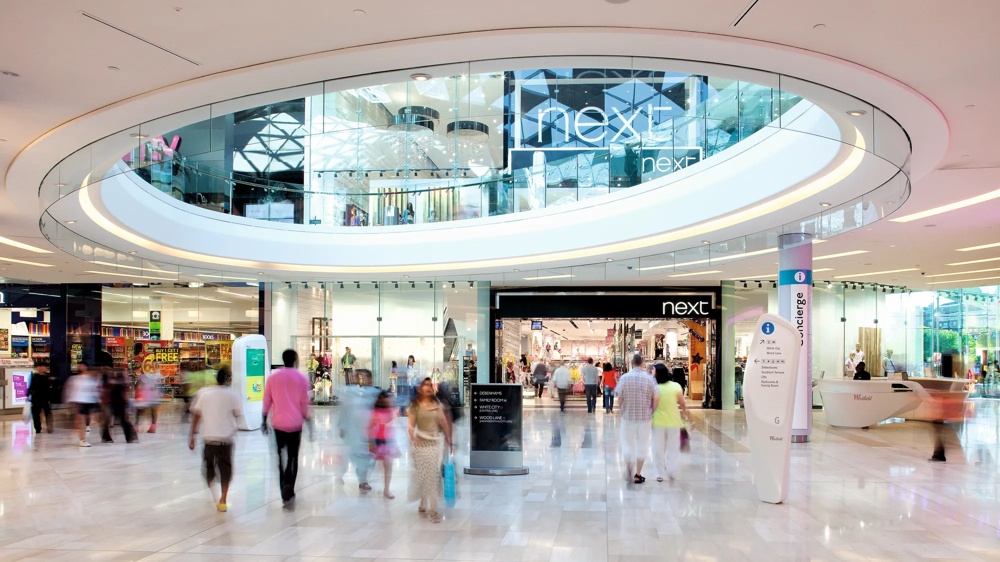 Menschen gehen in einem modernen Einkaufszentrum mit Geschäften und Glasfassaden spazieren.