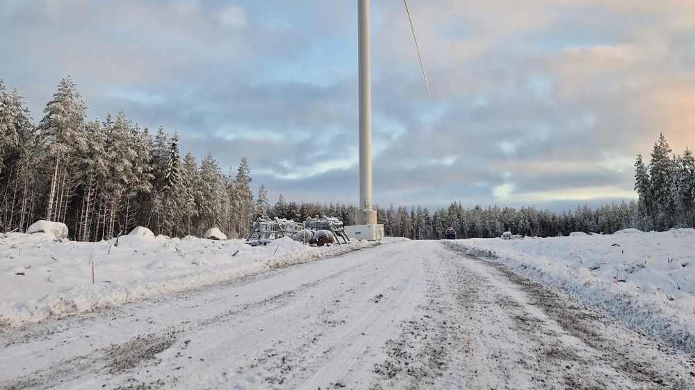 Ein Windrad steht in verschneiter Landschaft unter blauem Himmel mit Wolken.