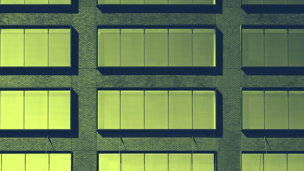 Fassade eines Gebäudes mit großen, gelb getönten Fenstern in gleichmäßigen Reihen auf Backsteinmauer.