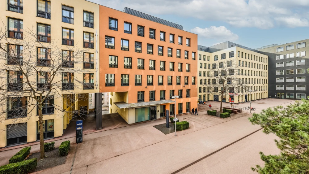 Several modern office buildings with colourful facades and bare trees on a cloudy day.