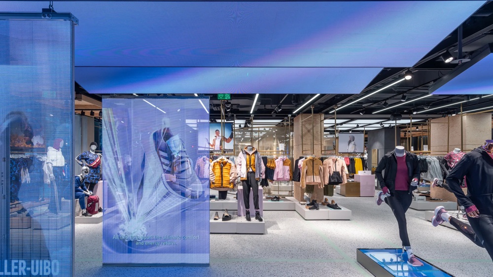 Moderner Bekleidungsladen mit Schaufensterpuppen, bunter Kleidung und digitalem Schuh-Display auf leuchtendem Boden.