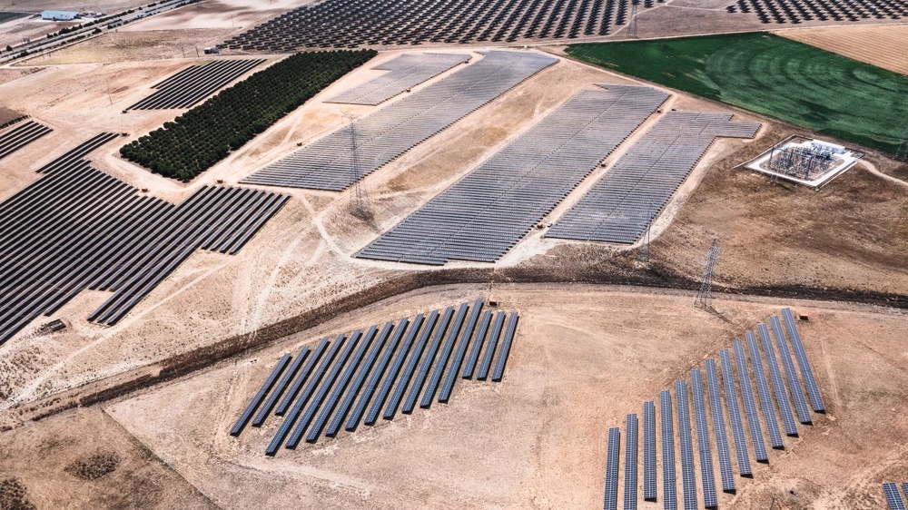 Luftaufnahme von Solarpanels auf einem trockenen Feld mit vereinzelten grünen Flächen.