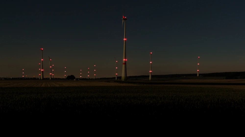 Wind farm with illuminated wind turbines at dusk above open fields, red warning lights against a dark evening sky, renewable energy.