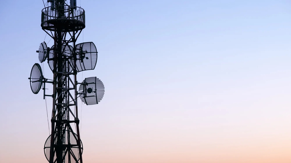 Ein Sendemast mit Antennen vor einem pastellfarbenen Sonnenuntergangshimmel.