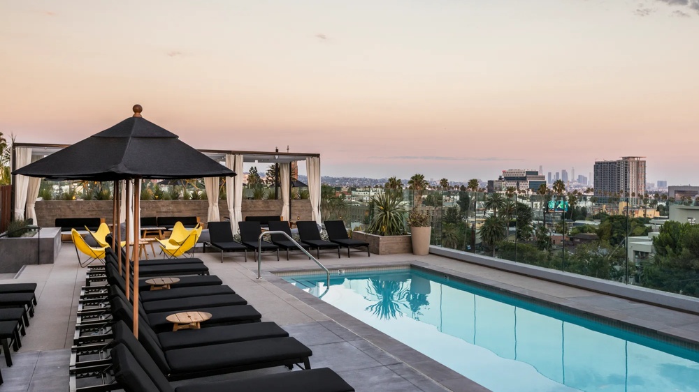 Dachterrasse mit Pool, schwarzen Liegestühlen, gelben Stühlen und Blick auf die Stadt bei Sonnenuntergang.