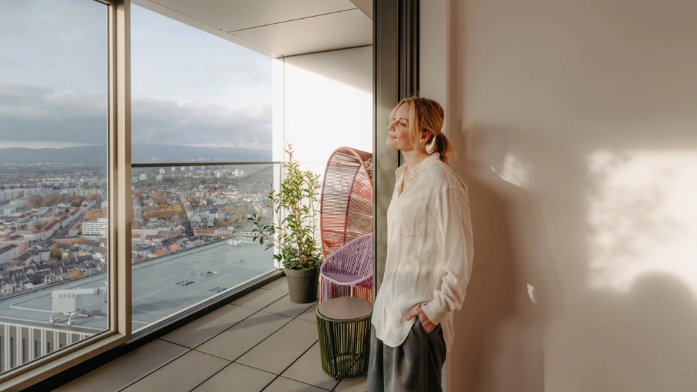 Frau steht auf einem Balkon mit Blick über die Skyline von Frankfurt.
