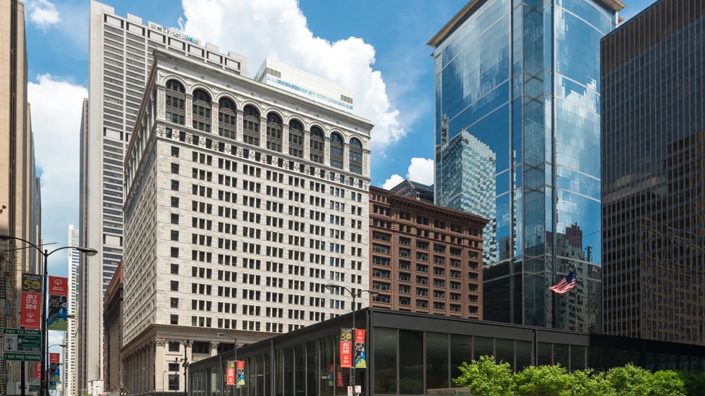 Hohe Gebäude in einer Stadt, darunter ein historisches weißes Gebäude und moderne Glasfassaden unter blauem Himmel.