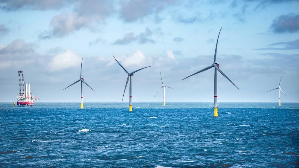 Windpark im Meer mit fünf Windturbinen und einem Schiff unter bewölktem Himmel.