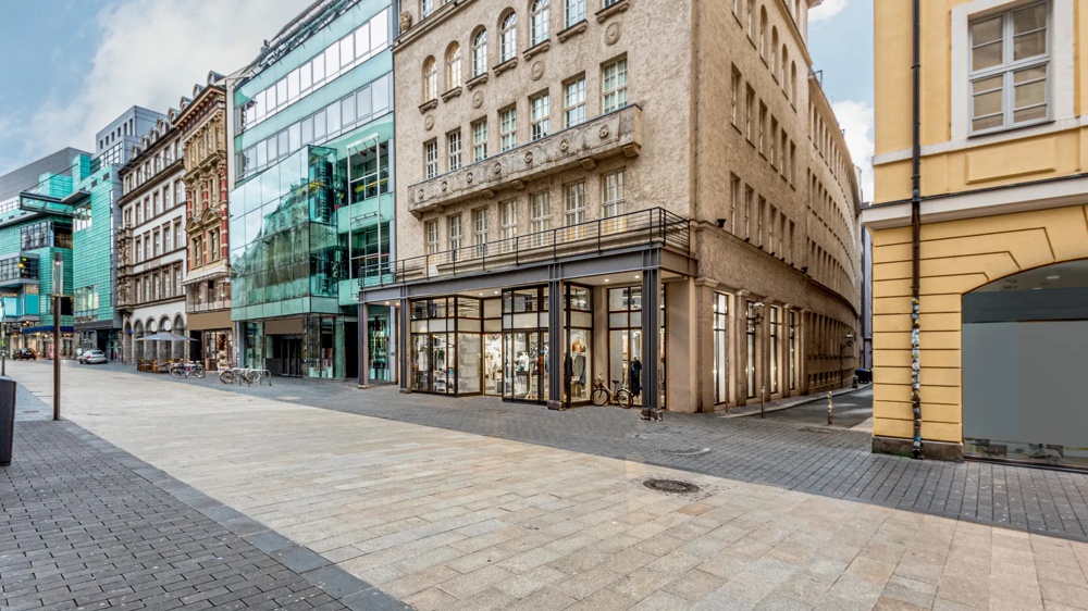 Ecke eines modernen Gebäudes mit Glasfassade neben einem älteren, verzierten Haus an einer leeren Straßenecke.