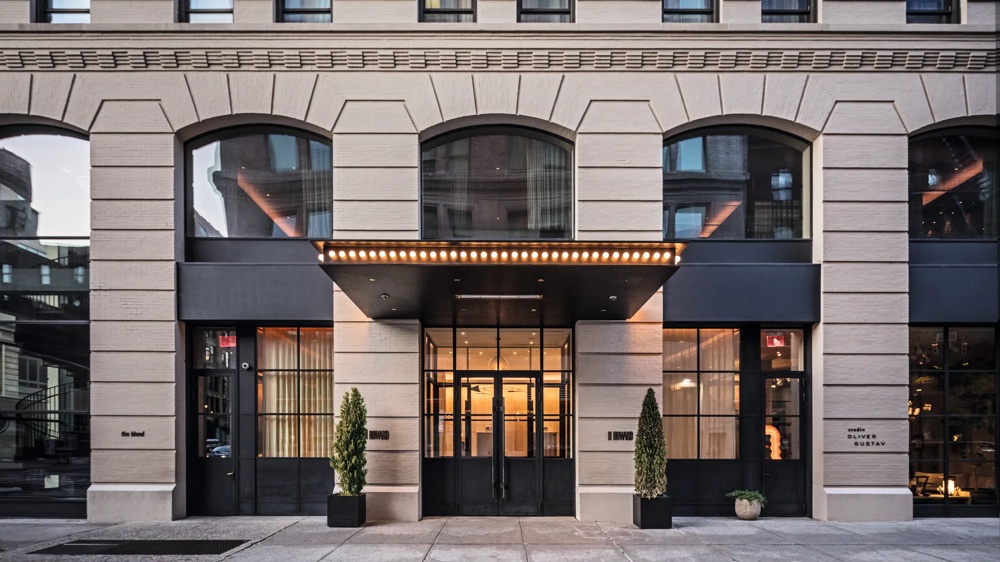 Eingang eines modernen Gebäudes mit großen Fenstern und zwei Pflanzen in schwarzen Töpfen.