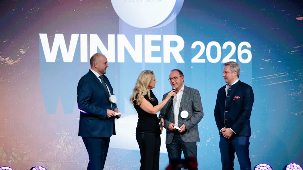 Vier Personen auf einer Bühne, eine Frau interviewt zwei Männer mit Trophäen, im Hintergrund steht 'WINNER 2026'.