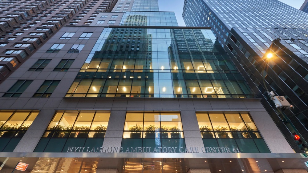 Glasfassade eines hohen Gebäudes mit reflektierenden Fenstern und beleuchteten Räumen bei Dämmerung.