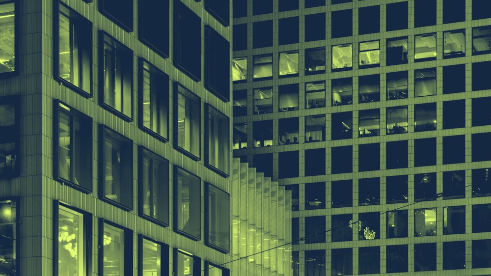 Moderne Gebäude mit vielen erleuchteten Fenstern bei Nacht, geometrische Strukturen und rechteckige Muster.