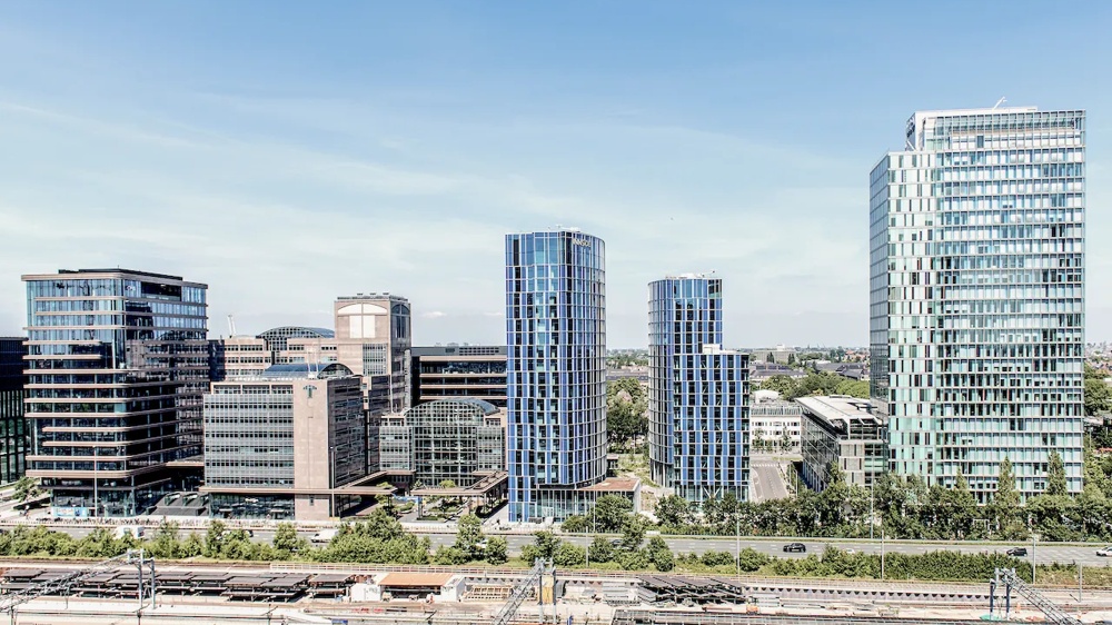 Moderne Hochhäuser mit Glasfassaden vor klarem Himmel, darunter eine Straße mit Bäumen.