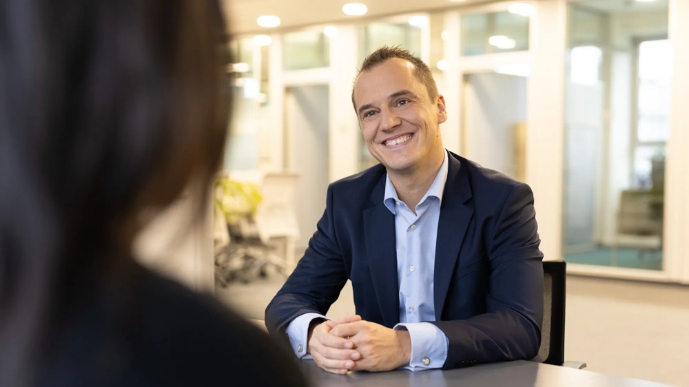 A man in suit smiling at a table in a modern office.