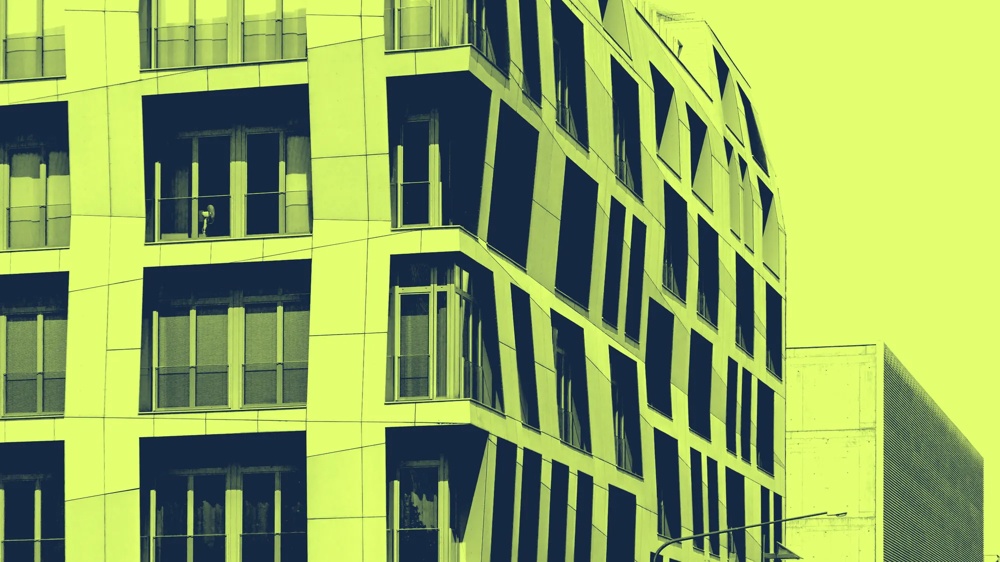 Modernes Gebäude mit unregelmäßigen Fenstern in gelb-grünem Farbton, seitliche Ansicht.