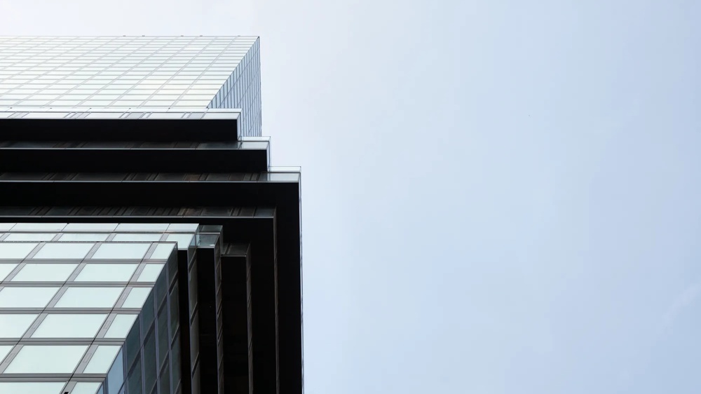 Ein modernes Gebäude ragt in den Himmel, mit Glasfassaden und gestaffelten Ebenen vor einem hellen Himmel.