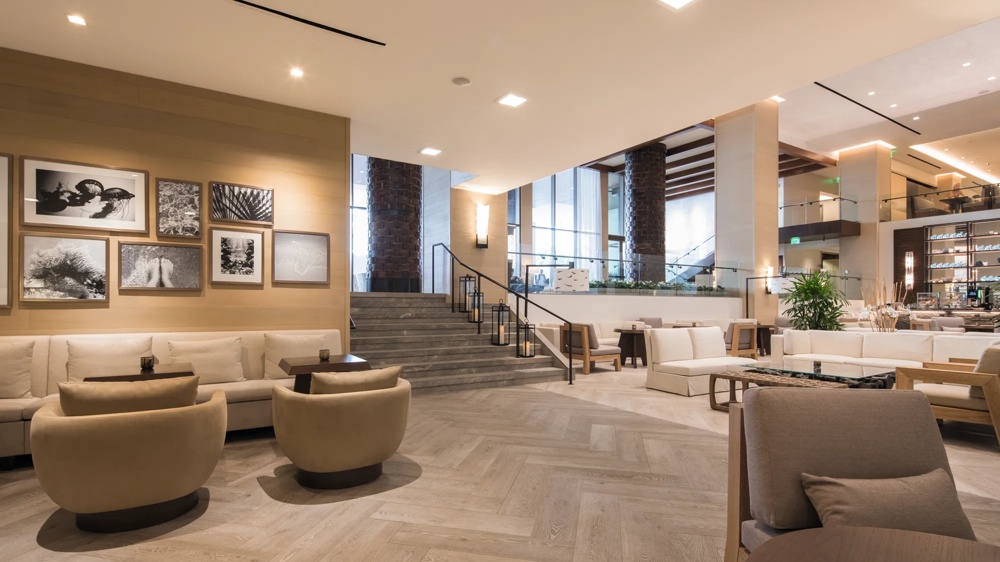 Großer, moderner Hotel-Lobbybereich mit Sofas, Sesseln, Kunstwerken an der Wand und Treppe im Hintergrund.