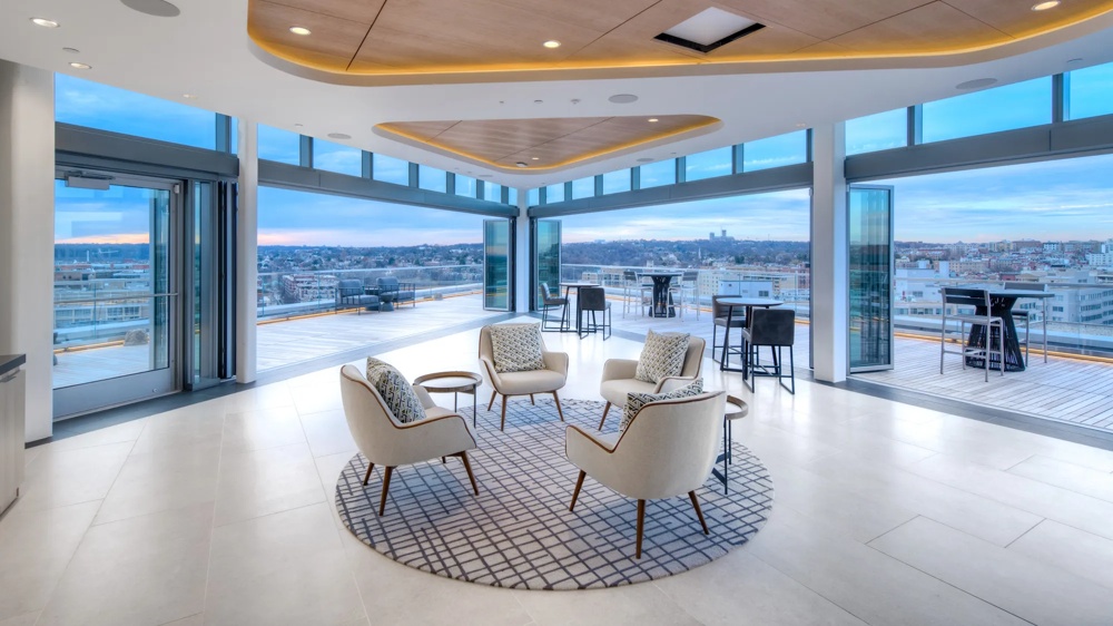 Moderner Raum mit Sesseln auf Teppich, großen Fenstern und Blick auf die Stadt bei Sonnenuntergang.