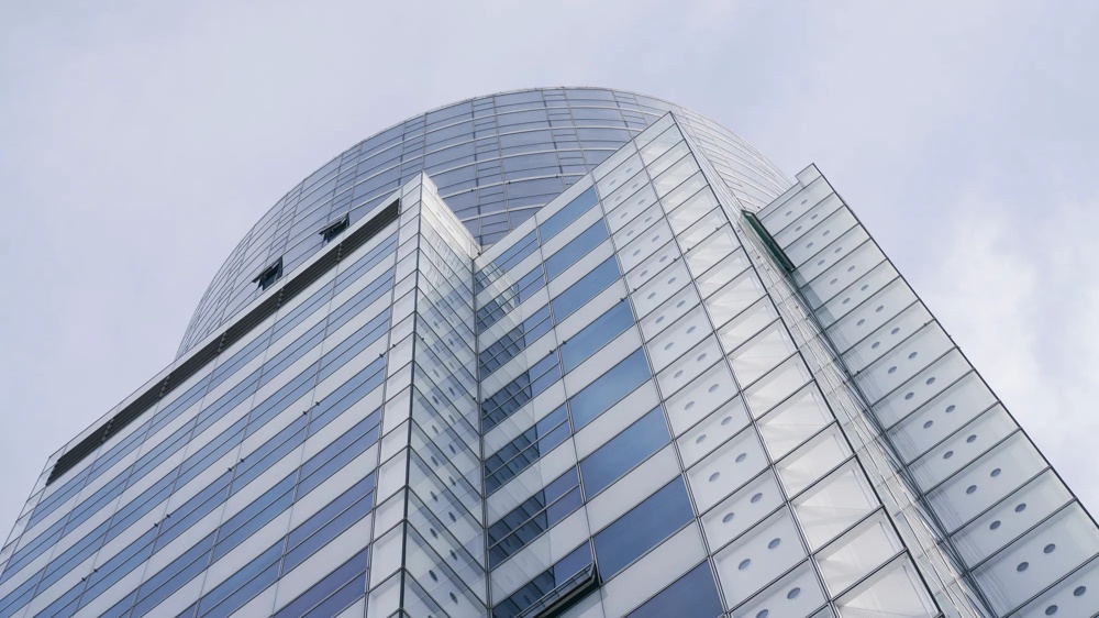 Modernes, hohes Gebäude mit Glasfassade vor bewölktem Himmel.