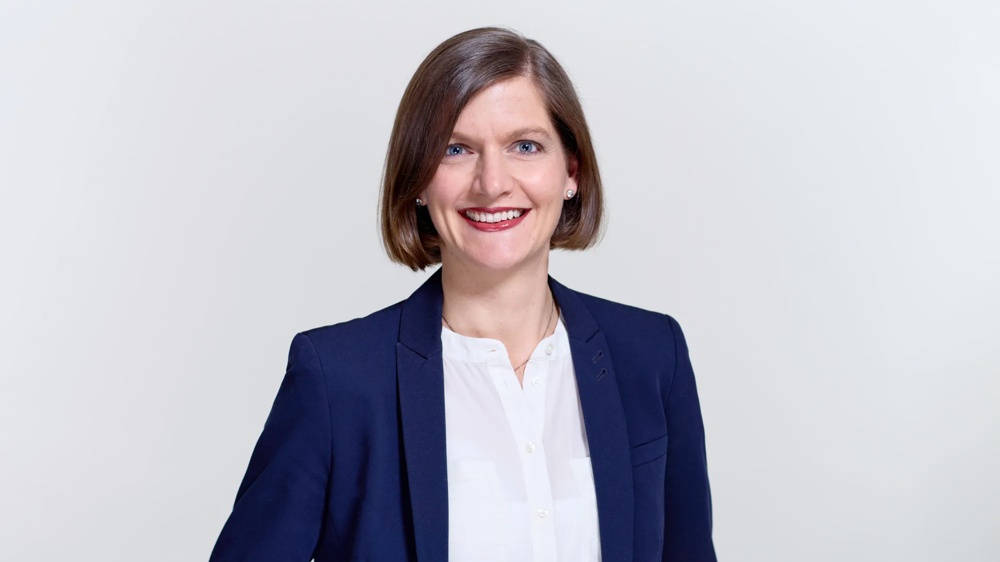 A smiling person in a blue blazer and white blouse against a light background.