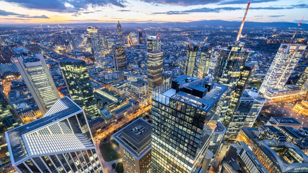 Blick auf eine beleuchtete Skyline einer Stadt bei Dämmerung mit vielen Hochhäusern und Straßen.