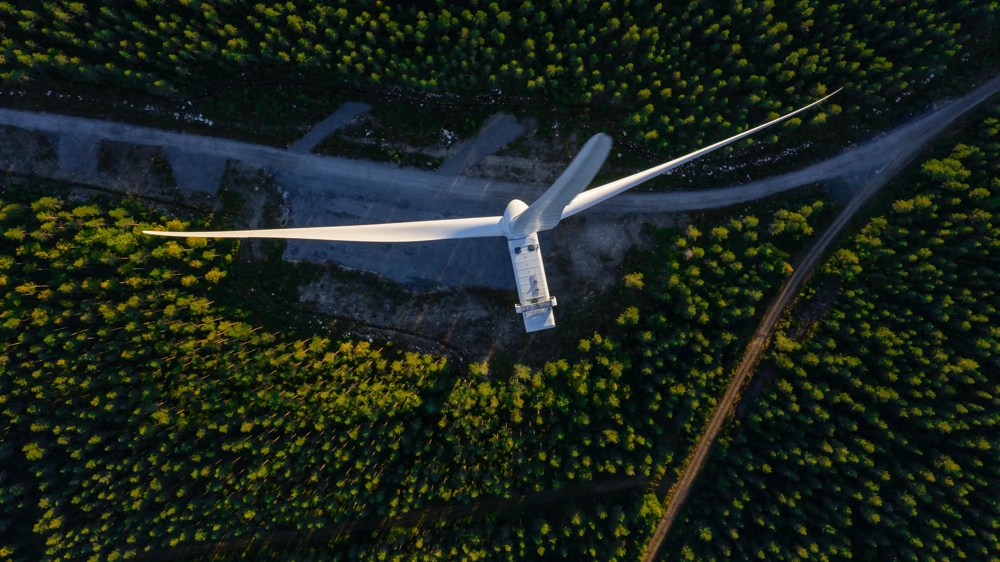 Windturbine von oben, umgeben von dichtem Wald und einem schmalen Weg.