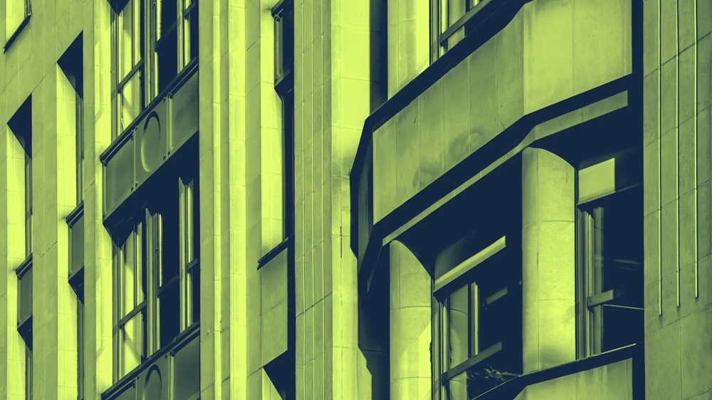 Fassadenansicht eines Gebäudes mit vertikalen Linien und Fenstern in grün-gelbem Ton.
