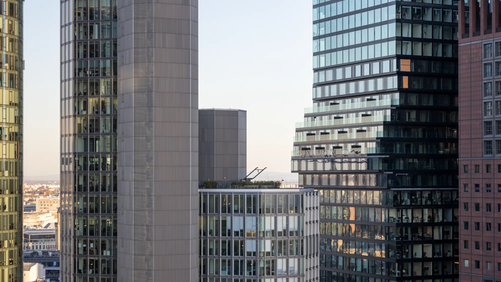 Several modern high-rise buildings with glass facades in daylight, blue sky in the background.