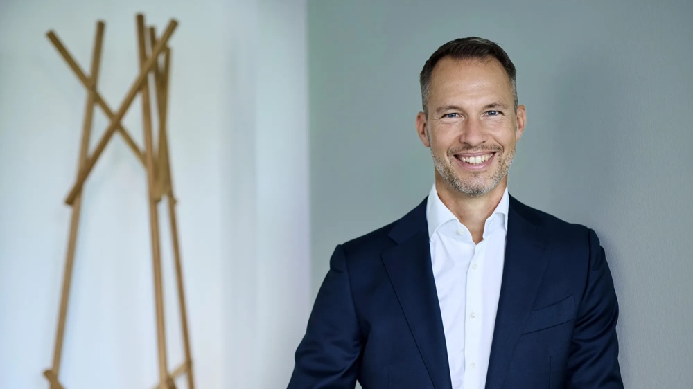 Michael Henn ist Global Head of Green Deal Infrastructure. Michael Henn lehnt gegen eine gruene Wand, neben ihm ist eine Metall-Skulptur.