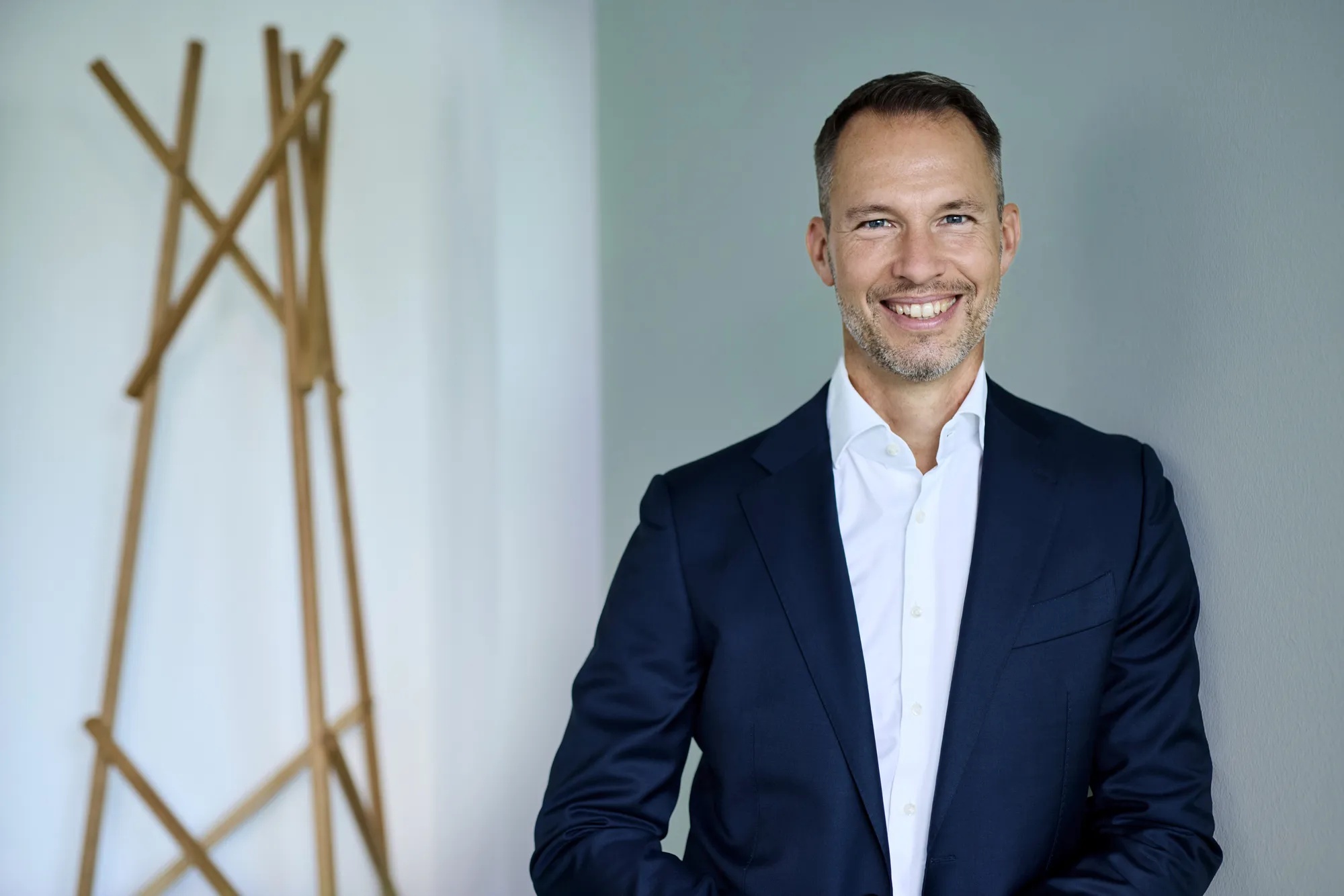 Michael Henn ist Global Head of Green Deal Infrastructure. Michael Henn lehnt gegen eine gruene Wand, neben ihm ist eine Metall-Skulptur.