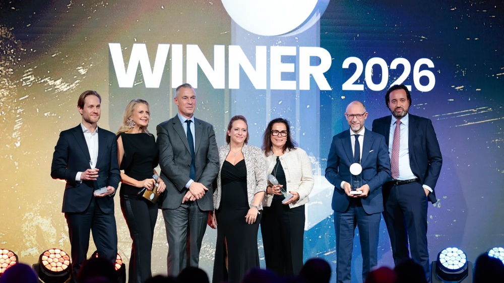 Eine Gruppe von sieben Personen in formeller Kleidung hält Trophäen vor einem Hintergrund mit der Aufschrift "WINNER 2026".