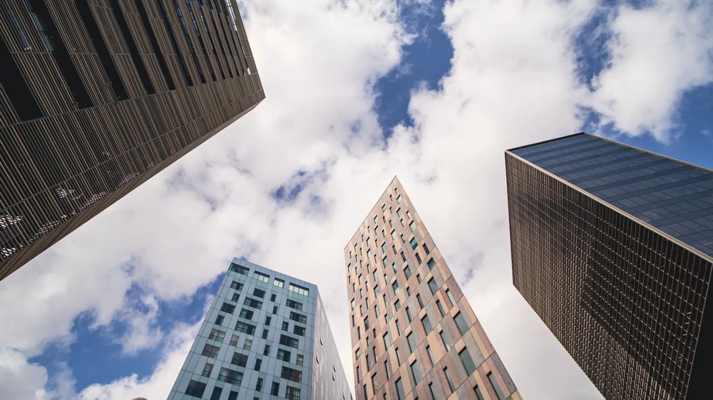 Hohe Gebäude ragen in den Himmel mit weißen Wolken und blauem Himmel im Hintergrund.