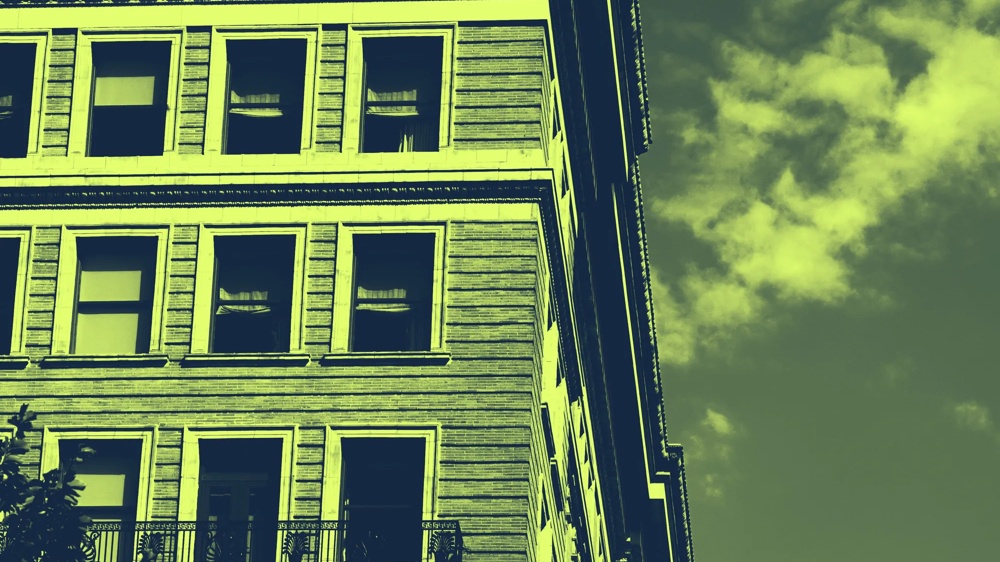 Fassade eines mehrstöckigen Gebäudes mit großen Fenstern und einem Balkon, vor einem bewölkten Himmel.