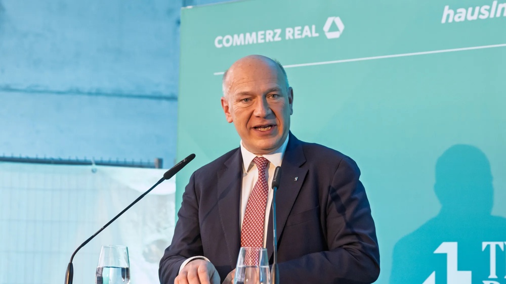 Redner steht am Pult vor gebrandeter Veranstaltungswand.