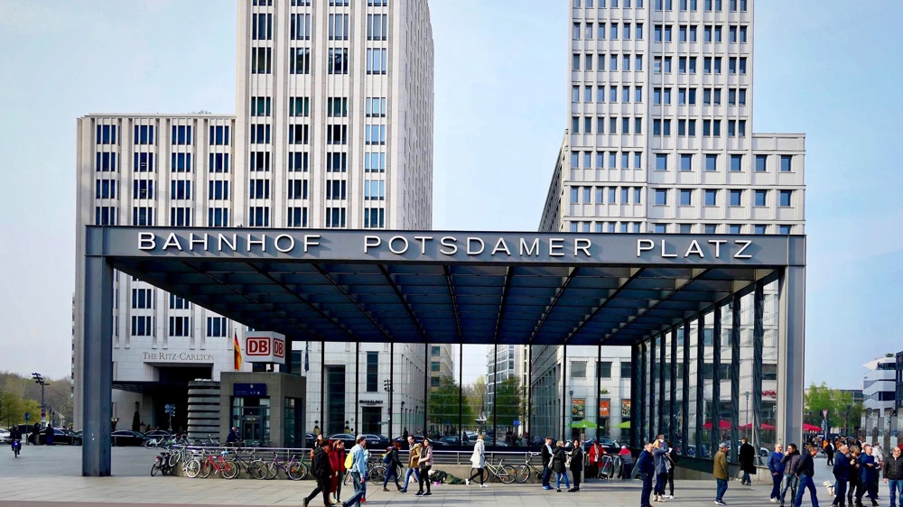 Eingang Bahnhof Potsdamer Platz, moderne Gebäude, Menschen und Fahrräder im Vordergrund.