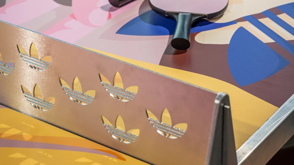 Zwei Tischtennisschläger auf einem bunt bemalten Tisch neben einem Netz mit ausgeschnittenen Logos.