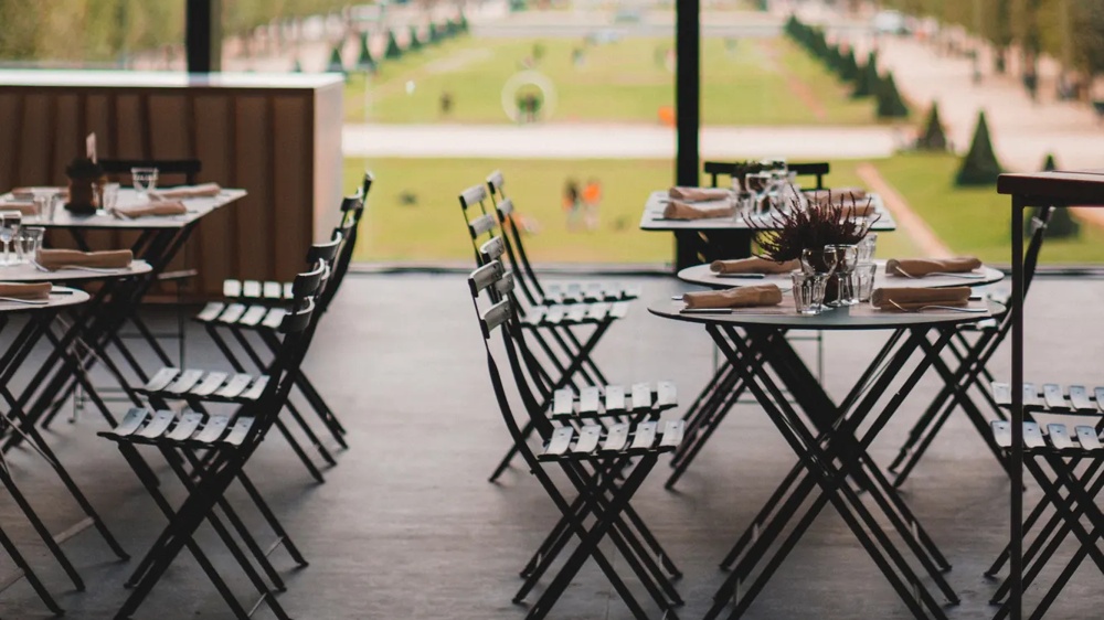 Ein Café mit Blick auf den Eiffelturm, Tische und Stühle im Vordergrund, große Fenster.