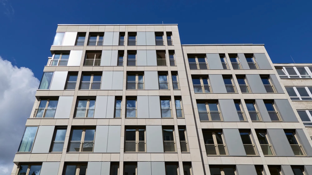 Fassadendetail der Büroimmobilie Schäfergasse 33 in Frankfurt am Main – Froschperspektive auf die strukturierte Naturstein- und Glasfassade vor blauem Himmel – ein hausInvest-Objekt.