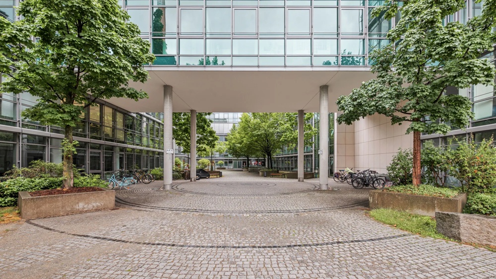 Gepflasterter Innenhof mit Bäumen, Fahrrädern und modernen Gebäuden aus Glas und Beton.