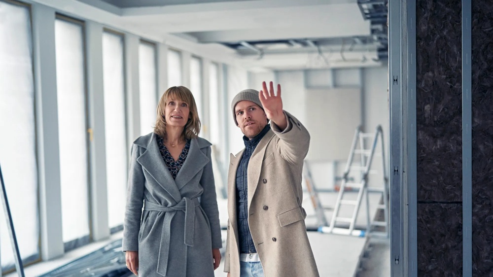Eine Frau mit schulterlangem Haar trägt einen grauen Mantel und schaut nach oben.